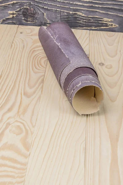 Papel de lija retorcido en un rollo se encuentra en una tabla de madera. Primer plano. Hay un tinte . —  Fotos de Stock