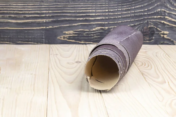 Sandpaper twisted into a roll lies on a wooden board. Close-up. There is a tint. — Stock Photo, Image