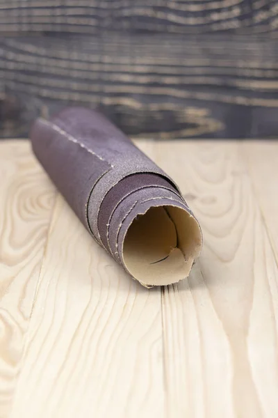 Papier de verre tordu en rouleau repose sur une planche de bois. Gros plan. Il y a une teinte . — Photo