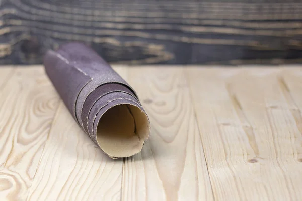 Papel de lija retorcido en un rollo se encuentra en una tabla de madera. Primer plano. Hay un tinte . —  Fotos de Stock