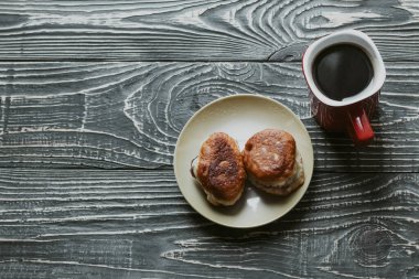 Koyu ahşap arka planda bir doku var. Bir fincan sade kahve ve içinde dolgu malzemesi olan ev yapımı hamur işlerinden iki çörek.