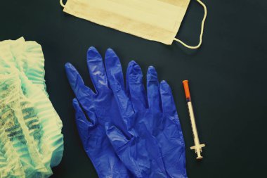dark background. On it lie medical gloves, a syringe, a cap, and a bandage on his face. Close-up. There is a tint