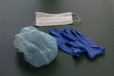 dark background. On it lie medical gloves, a syringe, a cap, and a bandage on his face. Close-up. There is a tint
