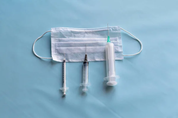 Máscara médica para proteção contra bactérias em um fundo azul. Perto de seringas para injectáveis. Close-up — Fotografia de Stock