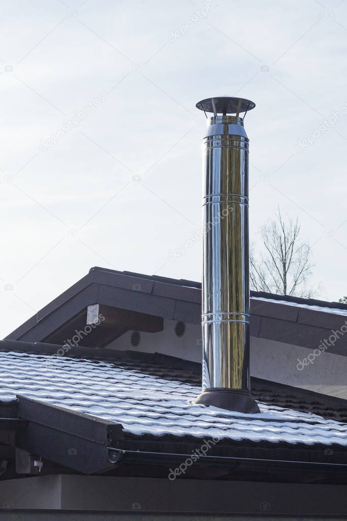 on open air. Stainless steel chimney on a dark roof. Not a lot of snow. Close-up.
