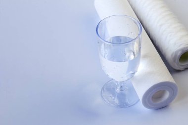 Su filtresi iki ünite. Bir bardak temiz suyun yanında. Beyaz arka plan, izolasyon yok. Yakın plan.