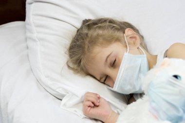 Beyaz saçlı kız yatakta yatıyor. Yüzünde tıbbi bir maske var. Yakın plan..