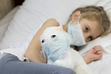 Yüzünde tıbbi maske olan beyaz saçlı bir kız. Yakınlarda, yüzündeki yumuşak oyuncak aynı zamanda bir öksürük maskesi. Yakın plan..
