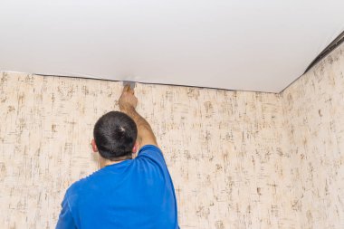 İşçi odada beyaz bir tavan çeker. Özel bir araç tüm kıvrımları eşitler.