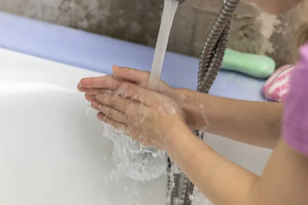 A child washes his hands in front of a faucet with water in the bathroom. Close-up.
