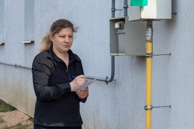 Köylü kadın duvarı kontrol edecek ve gaz sayacını bir deftere yazacak. Enerji tüketiminin analizi.