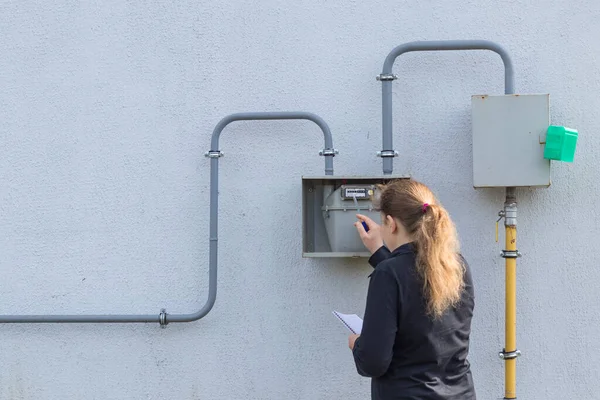 The girl the peasant woman will check on the wall and write down the gas meter in a notebook. Analysis of energy consumption. — Stock Image Girl Peasant Woman Check Wall Write Gas Meter Notebook Analysis Royalty Free Stock Images