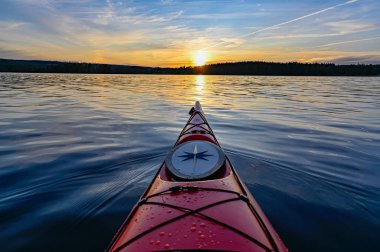 Günbatımında durgun suda kırmızı plastik kano.