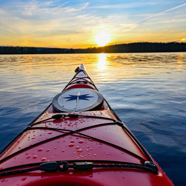 Günbatımında durgun suda kırmızı plastik kano.