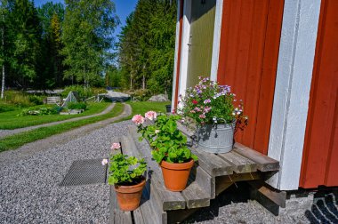 kırmızı ahşap bir kulübenin önündeki merdivenlerde çiçekler.