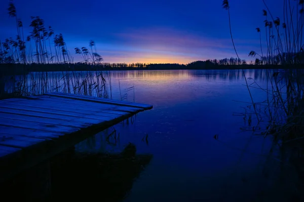 Sunrise over wooden jetty and frozen lake — Stock Photo, Image