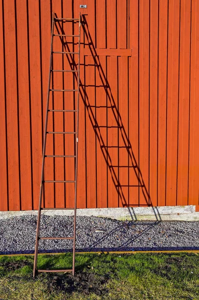 Ladder standing against a red house wall — Stock Fotó