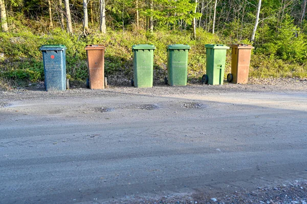 Seis botes de basura de pie cerca de la carretera de grava — Foto de Stock