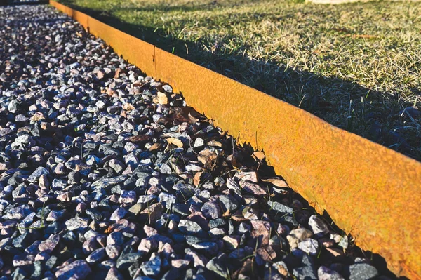 Rusty metal edge between grass and gravel — Stock Photo, Image