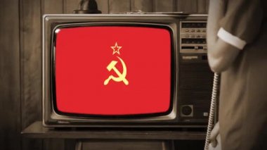 Evde Eski Telefonda Konuşan ve Retro TV 'de Kızıl Sovyetler Birliği Bayrağı İzleyen Genç Adam. Komünist Propaganda Konsepti. Sepia Tonu