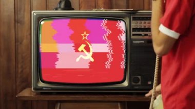 Evde Eski Telefondan Konuşan ve Retro TV 'de Kızıl Sovyetler Birliği Bayrağı İzleyen Genç Adam. 