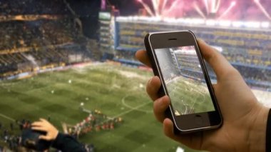 Buenos Aires / Arjantin - 09 09 09 2019: Bulanık Futbol Arkaplanı üzerinde eski akıllı bir telefon tutan erkek eller. Buenos Aires, Arjantin 'deki Bombonera Stadyumu' nda çekildi.. 
