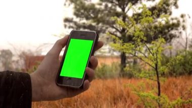 Fırtınalı bir günde kırsal alanda yeşil ekranlı eski akıllı bir telefon tutan erkek el. Sonraki Efektler ya da herhangi bir video düzenleme yazılımında Keying efekti ile yapabilirsiniz (YouTube 'daki derslere bakın).  