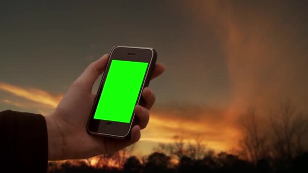 男性の手は日没時に緑の画面で古いスマートフォンを保持します 緑の画面を必要な映像や画像に置き換えることができます Effectsやその他のビデオ編集ソフトウェアのキーエフェクトで実行できます — ストック動画