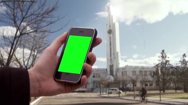 男性の手アルゼンチンの小さな町で緑の画面と古いスマートフォンを保持します 背景にある市役所の建物 緑の画面を必要な映像や画像に置き換えることができます キー効果でそれを行うことができます — ストック動画