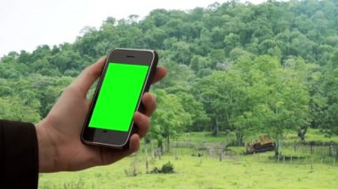 Ormanda Yeşil Ekran 'ı olan eski akıllı telefon kullanan bir adam. Yeşil ekranı istediğin görüntüyle ya da resimle değiştirebilirsin. Sonraki Efektler ya da herhangi bir video düzenleme yazılımında Keying efekti ile yapabilirsiniz (YouTube 'daki derslere bakın).  