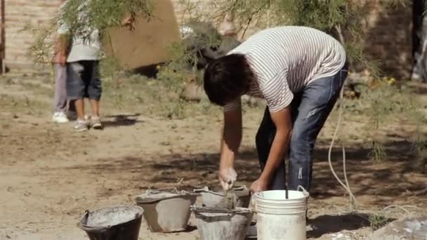 布宜诺斯艾利斯 一个人把水泥和水混在桶上 孩子们在一个贫穷的社区里玩背景游戏 — 图库视频影像