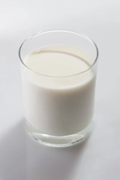 Vidro incolor cheio de leite de vaca no fundo branco — Fotografia de Stock