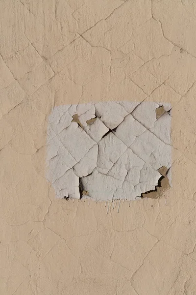 Verf op de muur van het gebouw van de huid. Scheuren op het oppervlak. Witte rechthoek op een beige muur — Stockfoto