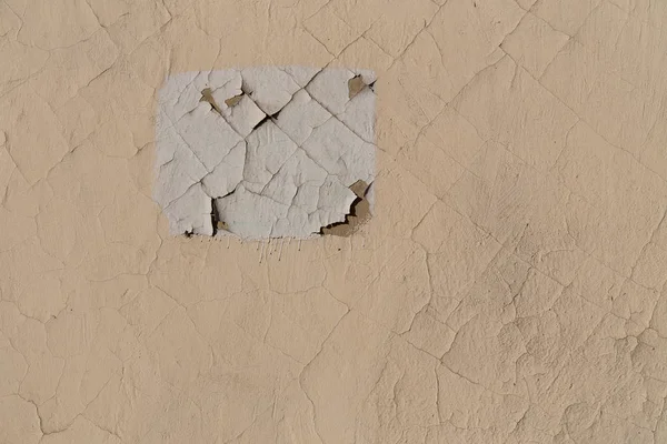 Pintura de piel en la pared del edificio. Grietas en la superficie. Rectángulo blanco en una pared beige — Foto de Stock