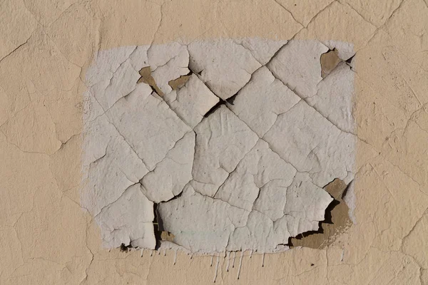 Vernice per la pelle sulla parete dell'edificio. Crepe sulla superficie. Rettangolo bianco su una parete beige — Foto Stock