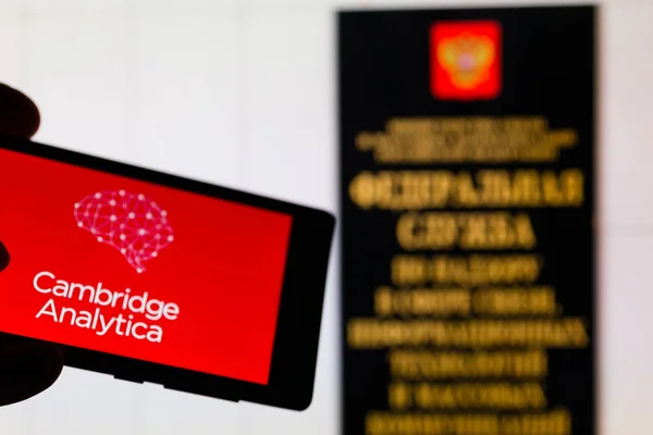 MOSCOW, RUSSIA - MAY 9, 2018: Smartphone in hand with Cambridge Analytica logo infamous after the leakage of personal data from Facebook. Entrance to Roskomnadzor office in background. GDPR concept. — Stock Photo, Image