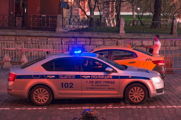 MOSCÚ, RUSIA - 30 DE ABRIL DE 2018: Un coche de policía con luces intermitentes y un taxi cerca de St. Catedral de Basilio en la Plaza Roja. Tarde, antes del atardecer — Foto de Stock