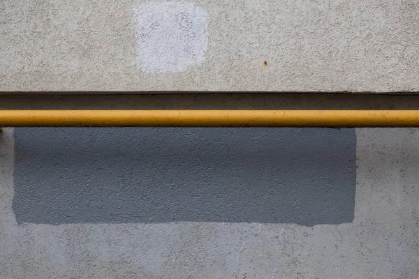 A horizontal gas pipe painted with yellow paint next to the building wall. Texture of concrete. Rectangle of gray paint over the spot of obscene graffiti. Graphic design neutral grunge background.