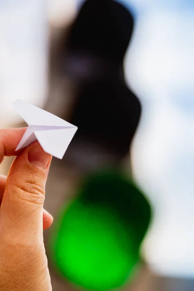 One small paper airplane in hand against a traffic light background with a glowing green signal. Permission to fly. Takeoff is approved and allowed. Vertical shot. Concept. — Stock Photo, Image