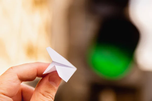 Bir küçük kağıt uçak ile bir parlayan ampul arka plan karşı elinde yeşil sinyal. Uçmak için izin istiyorum. Kalkış onaylanmış ve izin. Yatay Çerçeve. Kavramı