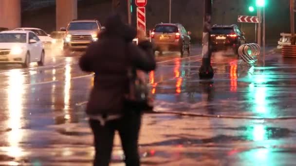 Жінка в куртці з капюшоном йде нічною вулицею під дощем. — стокове відео