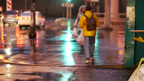 Ceket ve şemsiyeli insanlar sağanak yağmurda bir gece caddesi boyunca yürürler. — Stok video