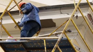 İnşaat işçisi bir binanın iskelesinde sıva dekoru yapıyor.