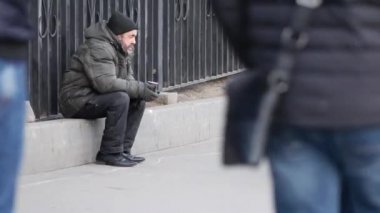 Kışlık montlu fakir yaşlı adam elinde tek kullanımlık bardakla sokakta oturuyor.
