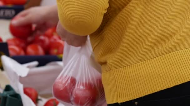 Comprador en el supermercado elegir tomates frescos. Mujer en blusa amarilla sostiene en h — Vídeos de Stock