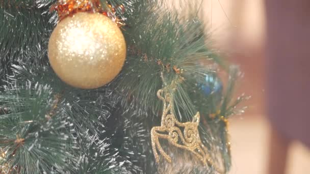 Árbol de Navidad con juguetes cerca. Bolas de Navidad doradas y azules. La gente camina en el fondo. Decoración de Año Nuevo. Árbol de Navidad tradicional . — Vídeo de stock