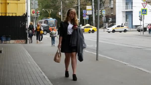 Ludzie chodzą ulicami miasta. Dziewczyna idzie chodnikiem z telefonem. — Wideo stockowe