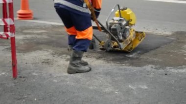 Turuncu korumalı üniformalı bir adam yeni asfalt kaldırım döşedi.