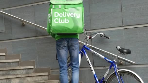 Courier in uniform and branded green delivery club backpacks with bike on steps. — Stock Video