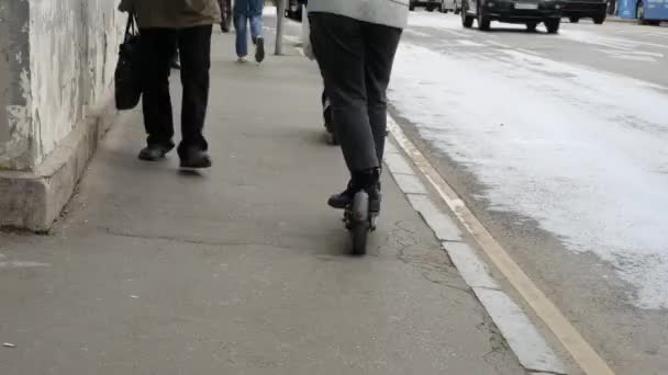 Um cara monta uma scooter elétrica ao longo da calçada. Um autocarro está a passar — Vídeo de Stock
